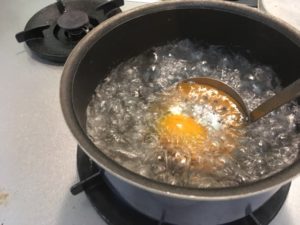 沸騰した鍋の湯の中にミニトマトをお玉にのせて入れる